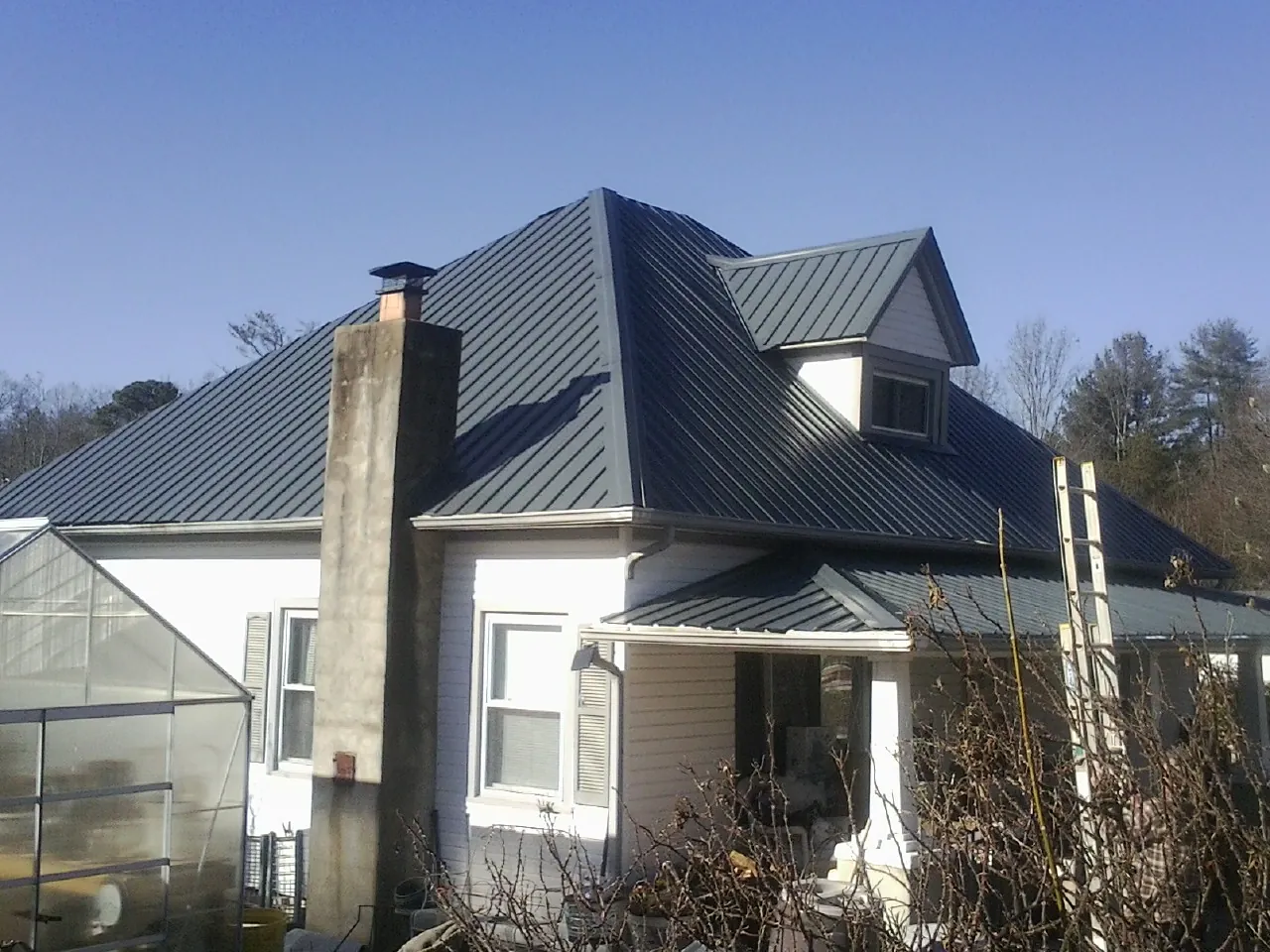 Dark blue standing seam metal roof on a white farmhouse with dormer — Slate & Tile Roof Repair by Roofing Brothers in Hampstead