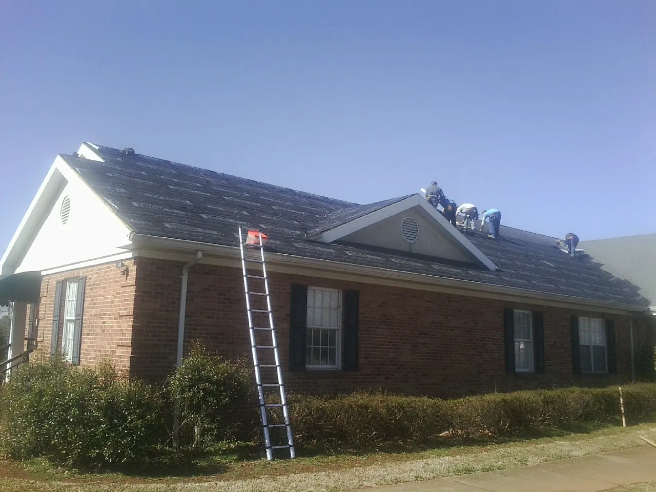 Crew tearing shingles off a brick ranch roof with a ladder set — Metal Roof Repair work by our crew in Hampstead