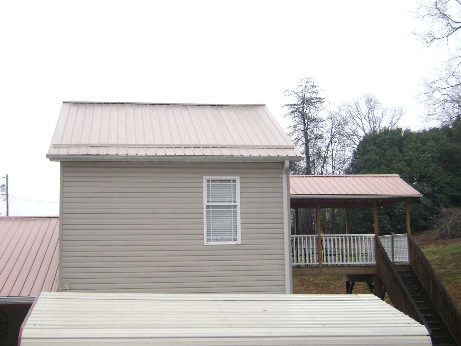 Tan metal roofs on a two story addition and attached porch, from a Roof Replacement job in Hampstead